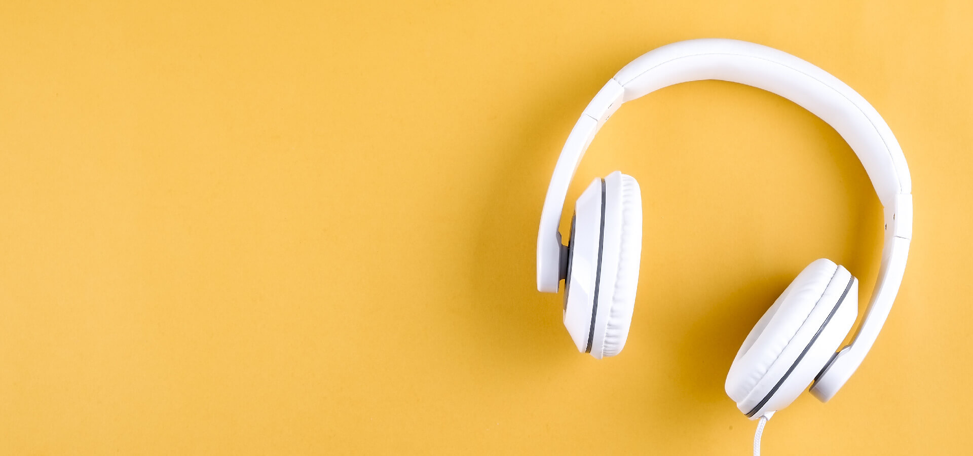 Overhead photo of white headphone sitting on yellow desk